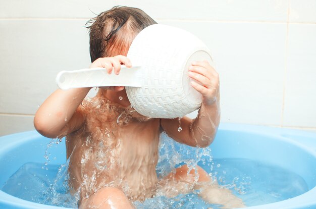 Garoto feliz tomando banho, despeje água com um balde branco