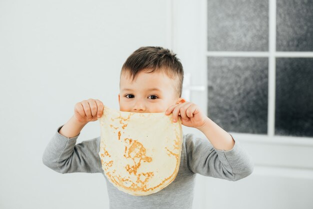 Garoto fofo segurando uma panqueca na boca, brincando de fofo