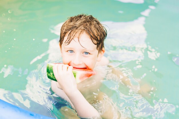 Garoto garoto comendo melancia sorrindo nadando na piscina no verão crianças com um pedaço de melancia