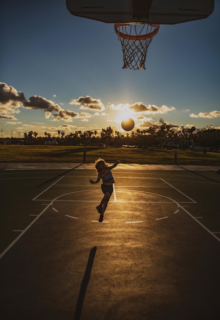 Garoto jogando basquete menino bonitinho pulando com bola de basquete para silhueta de tiro no pôr do sol