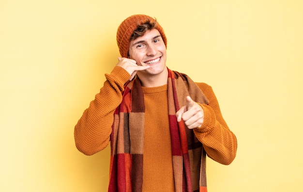 Garoto jovem adolescente sorrindo alegremente e apontando para a câmera enquanto faz um gesto depois de ligar para você, falando ao telefone