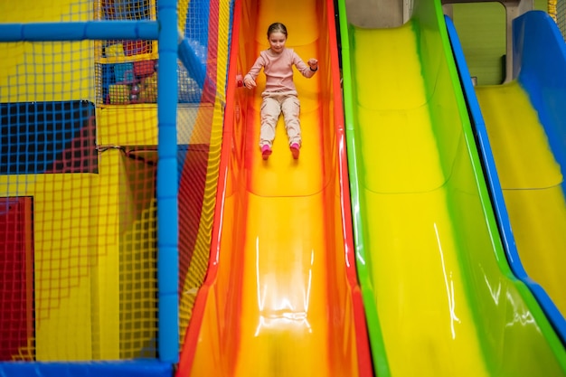 Garoto linda garota monta um slide no parque infantil trampolim criança feliz em movimento durante o entretenimento ativo.