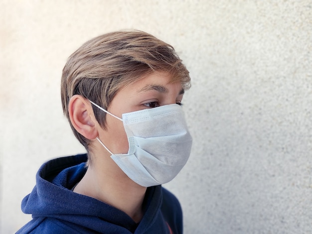 Garoto loiro adolescente usando máscara facial de medicina para proteção contra vírus