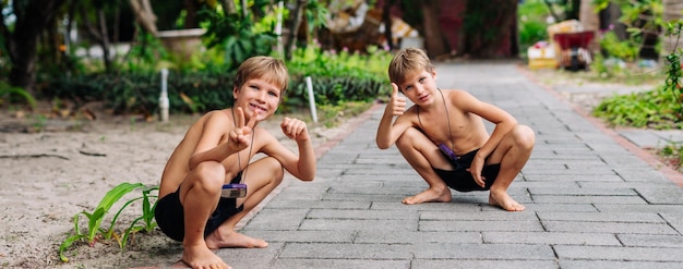 Foto garoto louro sardas agachados sentado sorrindo mostra gesto polegares para cima sem camisa calções de peito nu natureza