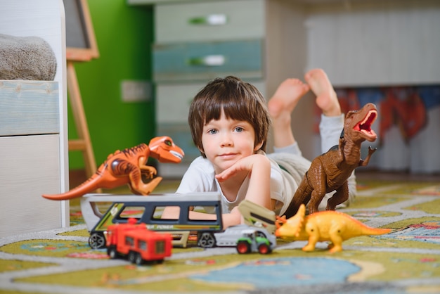 Garoto menino bonitinho brincando com muitos carros de brinquedo internos. Pré-escolar feliz se divertindo em casa ou no berçário