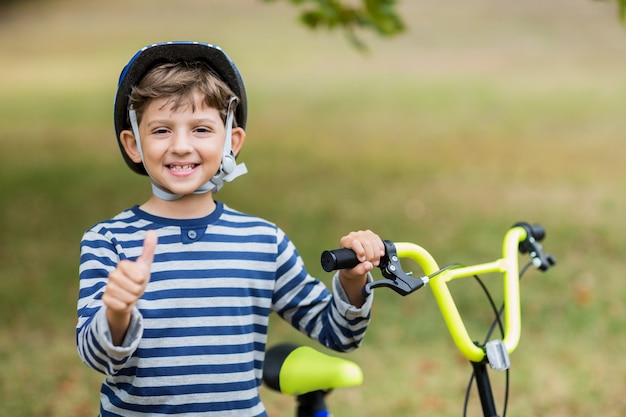 Garoto mostrando os polegares para cima em pé ao lado da bicicleta