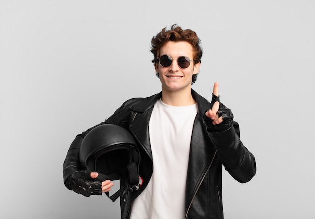 Garoto motociclista sorrindo e parecendo feliz, despreocupado e positivo, gesticulando vitória ou paz com uma mão