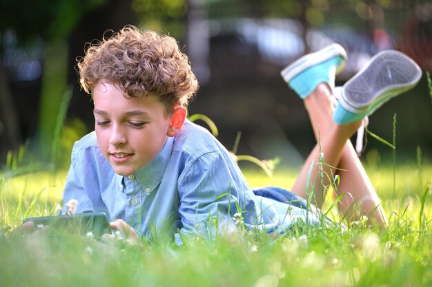 Garoto navegando em seu smartphone ao ar livre no parque de verão usando o celular para o conceito de lazer e educação