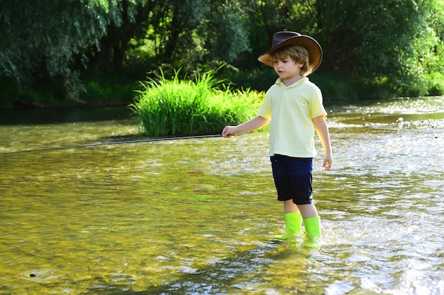 Garoto pescando em um rio da floresta Garoto de camisa amarela com uma vara de pescar à beira do rio Crianças Pescador de chapéu