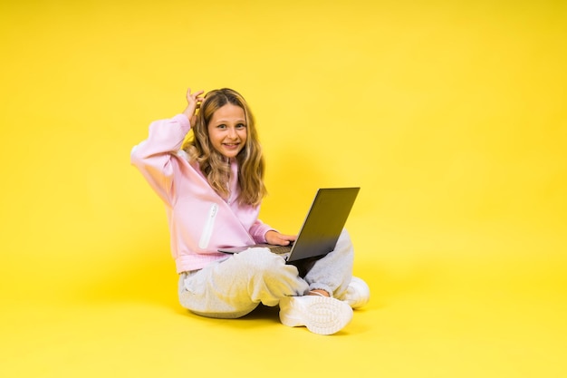 Garoto positivo senta-se com laptop lendo lição de casa usa pano de estilo casual isolado sobre fundo amarelo