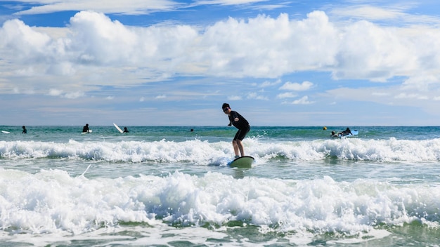 Foto garoto primeiro sucesso e fica em uma prancha macia enquanto pratica surfe em uma aula para iniciantes adolescente se equilibrando ativamente em equipamentos de esportes aquáticos e tentando novas experiências