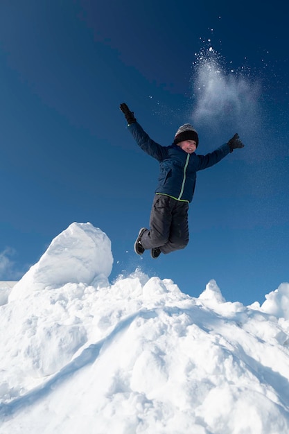 Garoto pulando em uma montanha de neve