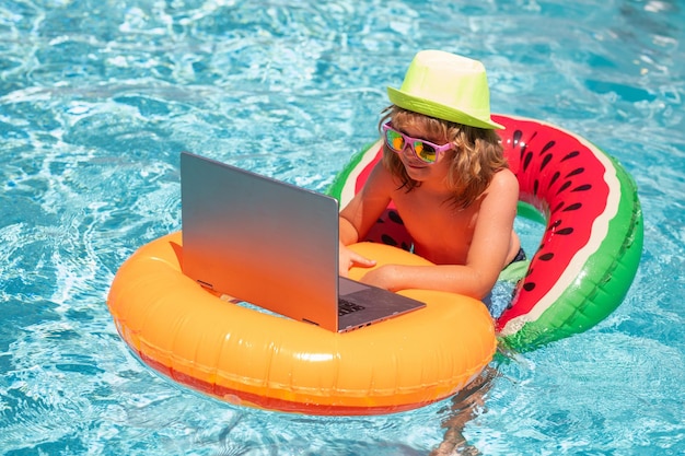 Garoto relaxando na piscina usando laptop no estudo on-line de crianças aquáticas de verão ou trabalhando em