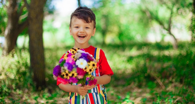 Garoto rindo com um buquê de flores uma criança com um buquê de flores silvestres para a mãe um presente uma surpresa com suas próprias mãos garoto emocional com flores em roupas brilhantes na natureza