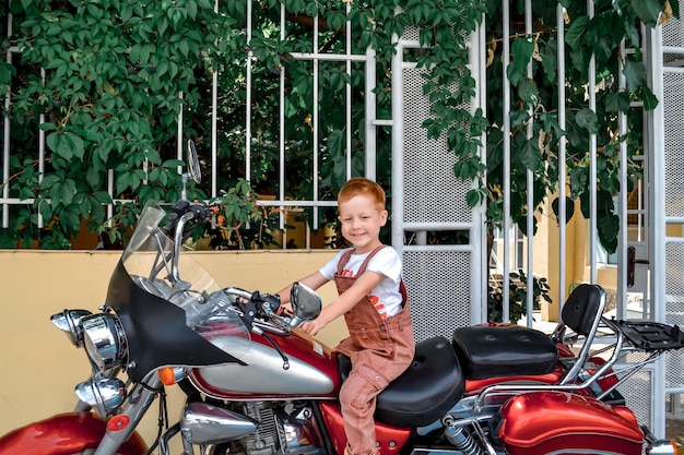 Foto garoto ruivo bonito senta-se em uma grande recreação de verão de motocicleta e retrato de estilo de vida de entretenimento