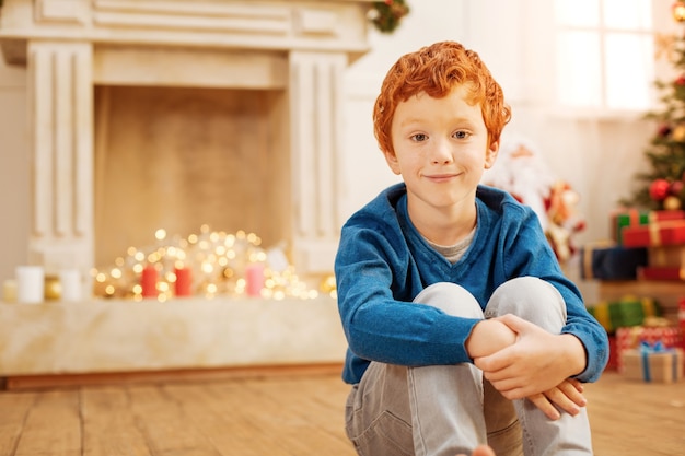 Garoto ruivo encantador com um leve sorriso no rosto enquanto espera sua família acordar e abrir os presentes de natal juntos.