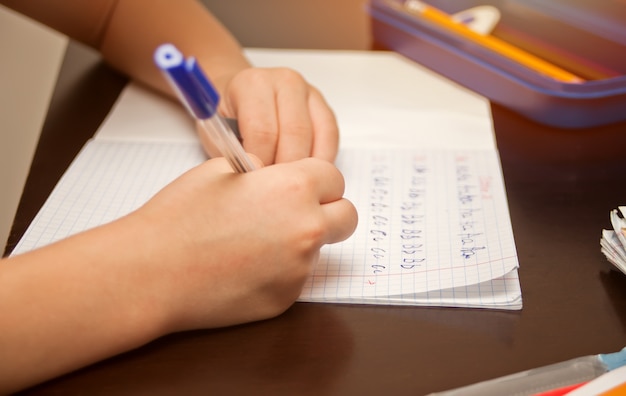 Foto garoto segurando a caneta e escrevendo no caderno