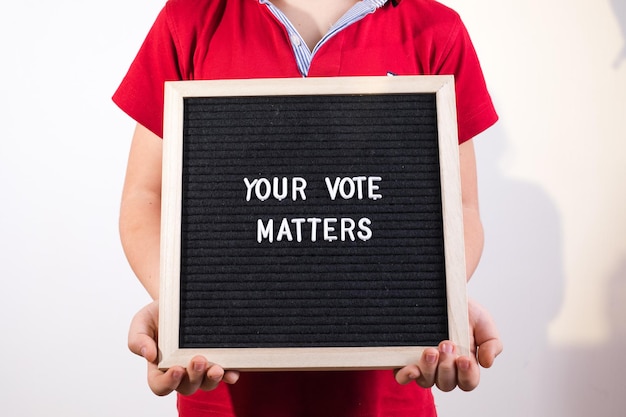 Garoto segurando o quadro de cartas com o texto Your Vote Matters em fundo branco