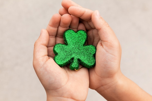 Foto garoto segurando um trevo brilhante verde nas mãos no dia de saint patricks