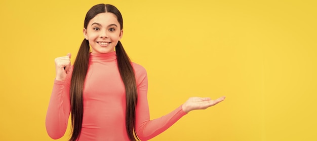 Garoto sorridente apresentando espaço de cópia de produto muito adolescente anunciando em fundo amarelo Cartaz horizontal de rosto de criança garota adolescente isolado banner de retrato com espaço de cópia