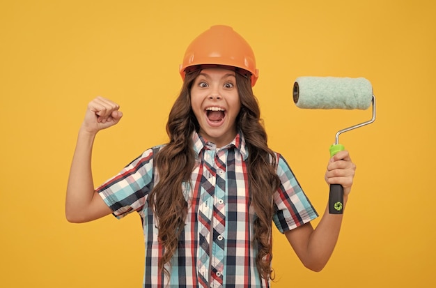 Garoto surpreso com cabelo encaracolado no capacete de construção segura a decoração do rolo de pintura