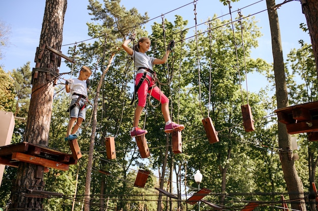 Garotos corajosos em escaladas de equipamento no parque de corda, playground. Crianças subindo em ponte suspensa
