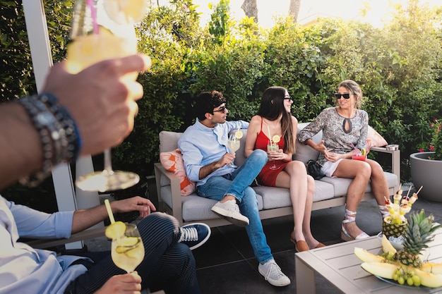 Garotos e garotas felizes despreocupados bebendo mocktails de sucos de frutas saudáveis no jardim do resort Conceito de estilo de vida com amigos caucasianos se divertindo juntos na tarde de verão relaxe o tempo