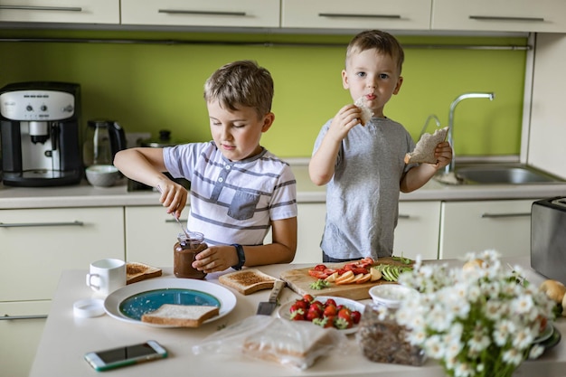 Garotos engraçados fazendo sanduíches com queijo cottage e pasta de chocolate na cozinha