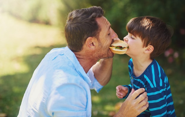 Garotos grandes dão grandes mordidas Foto recortada de um pai e filho comendo um hambúrguer do lado de fora