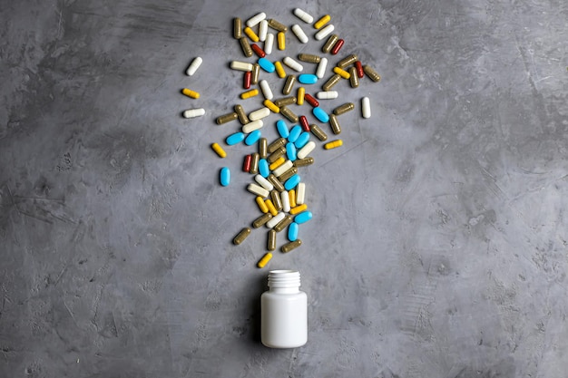 Garrafa branca e pílulas multicoloridas Fundo de concreto cinza Conceito de produtos farmacêuticos