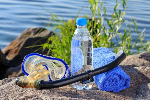 Garrafa com água, toalha, máscara para mergulho e tubo snorkel na rocha com fundo da costa do mar. Verão, estilo de vida ativo