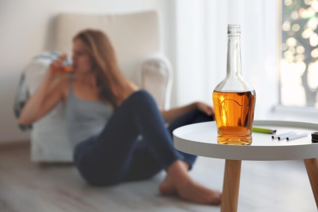 Garrafa com álcool na mesa e mulher bêbada no fundo