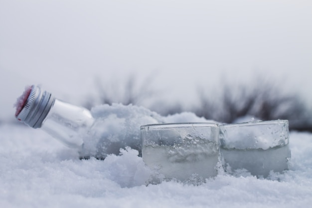 Garrafa com copos de vodka deitada no gelo