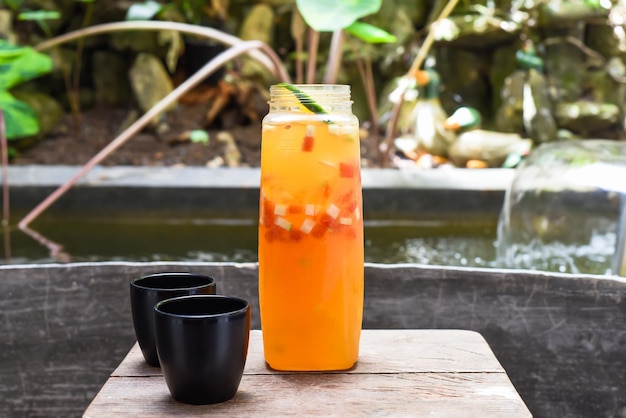 Garrafa com suco caseiro fresco feito de laranja, melancia, limão na mesa de madeira com xícaras