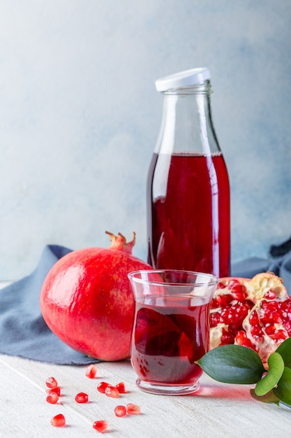 Garrafa com suco de romã e um copo, romã madura, inteira e descascada em um branco de madeira