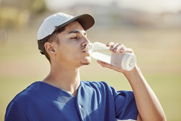Garrafa de água fitness e atleta bebendo líquido para sede, hidratação e saúde durante o treinamento Exercício esportivo e jogador de beisebol desfrutando de uma bebida refrescante enquanto praticava em um campo ao ar livre