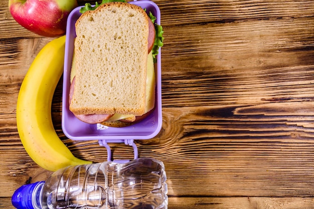 Garrafa de banana de maçã madura de água e lancheira com sanduíches em uma mesa de madeira Vista superior