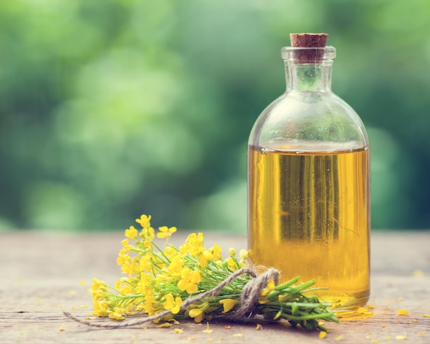 Garrafa de canola de óleo de colza e flores de estupro na mesa ao ar livre