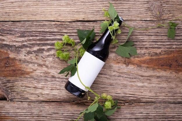 Garrafa de cerveja encontra-se sobre fundo de madeira com cones de lúpulo de perto Maquete de etiqueta branca