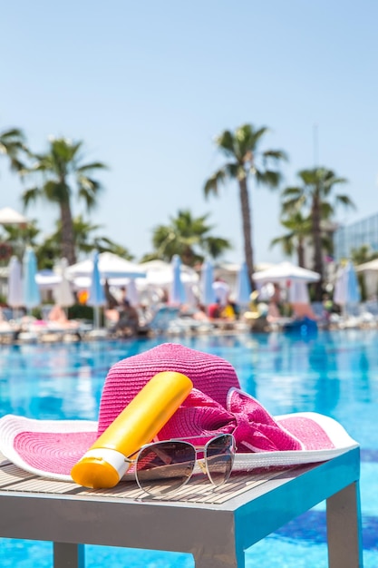 Garrafa de chapéu de protetor solar e óculos de sol ao lado da piscina no hotel