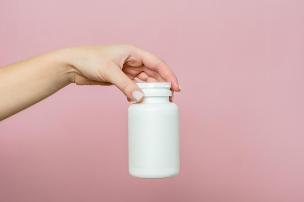 Garrafa de comprimidos ou vitaminas na mão de uma mulher Embalagem branca para a sua pílula ou cápsula e suplemento