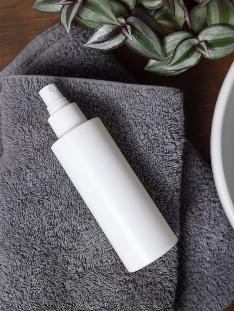 Garrafa de cosméticos de spray branco em toalha dobrada cinzenta perto de planta verde em madeira em maquete de banheiro