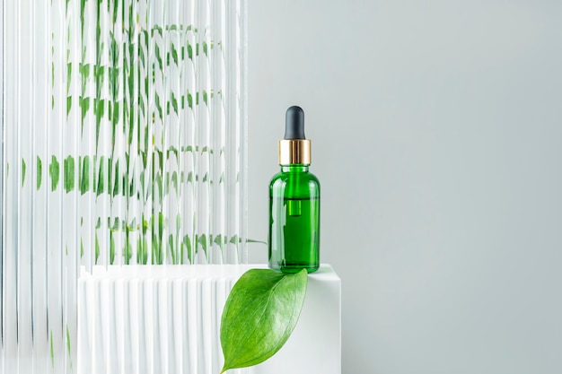 Garrafa de cosméticos de vidro verde com um gotinho em um fundo de plexiglas com folhas tropicais Conceito de cosmética natural Óleos essenciais naturais e produtos de cuidados com a pele