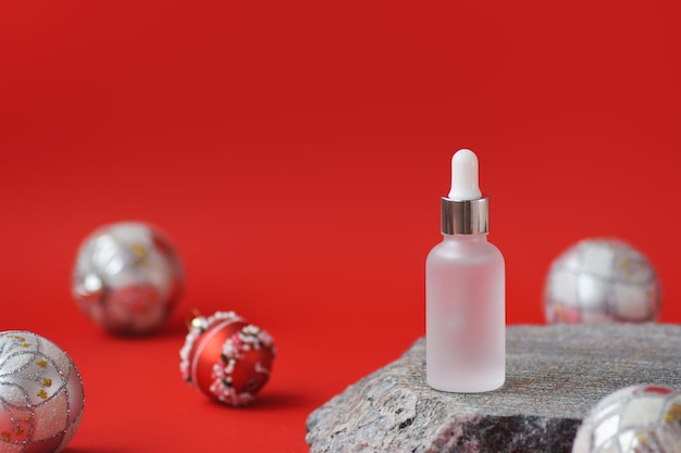 Garrafa de gotejador de vidro cosmético em pedra de mármore com bolas de Natal em foco suave em fundo vermelho