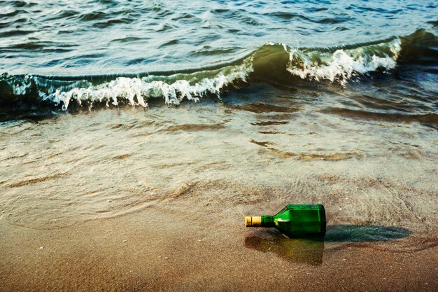 Garrafa de mensagem na praia em ondas