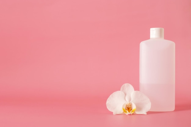 Garrafa de plástico branca para desinfetante para as mãos com flor de orquídea isolada em fundo rosa