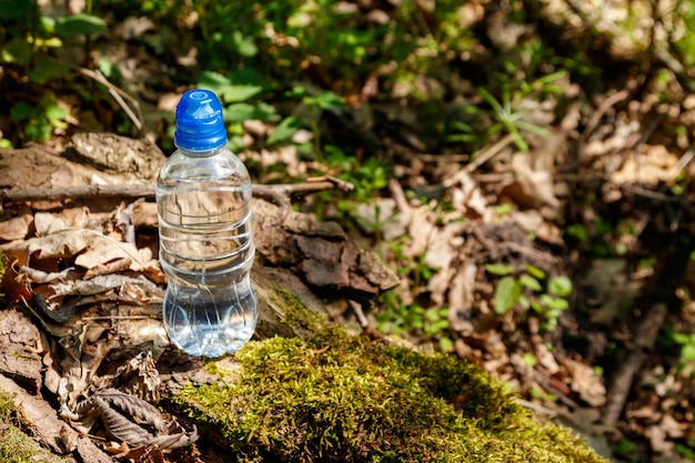 Garrafa de plástico com água potável fresca no fundo da floresta verde