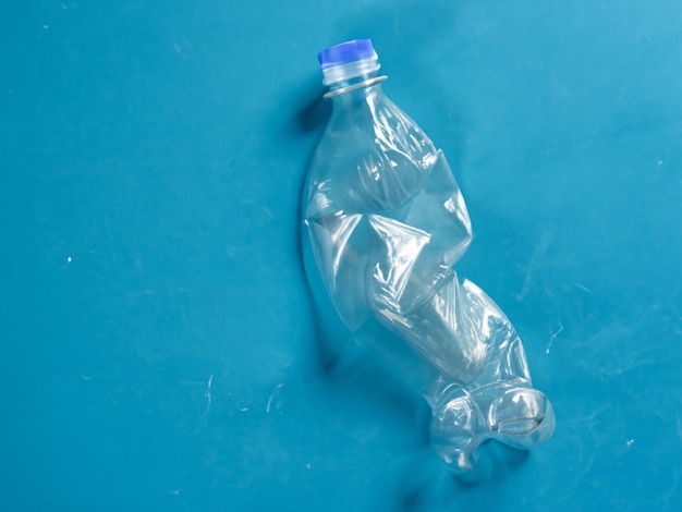 Garrafa de plástico usada vazia e amarrotada sobre fundo azul Espaço para cópia de vista superior Poluição ambiental