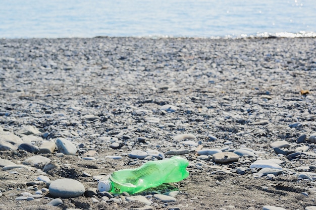 Foto garrafa de plástico verde amassada em uma praia de seixos, conceito de proteção ambiental, imagem horizontal de fundo de imagem de estilo de vida