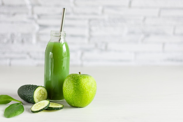 Garrafa de smoothie verde de desintoxicação feito com espinafre de maçã e pepino na mesa de madeira branca